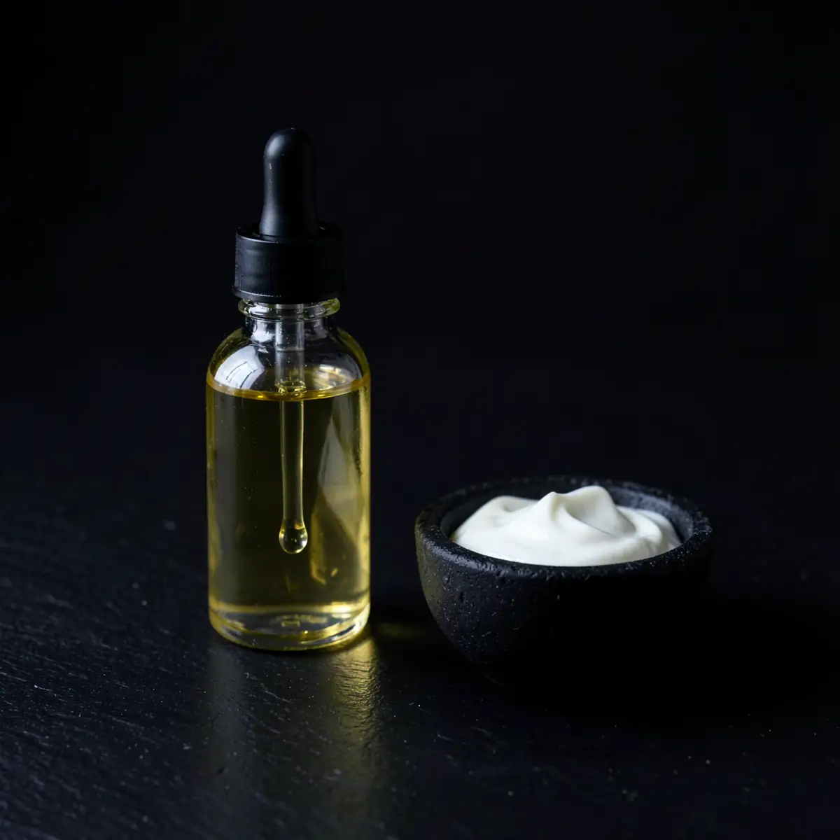 A glass dropper of golden hair oil beside a bowl of conditioning cream on black slate (illustrative, generated).